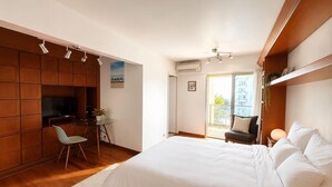 Ein Schlafzimmer mit Bett, Schreibtisch, Stuhl, Fernseher und einem Balkon.