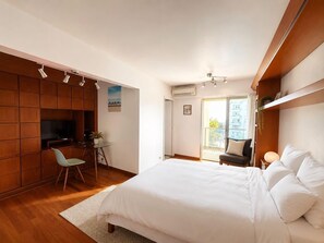 Ein Schlafzimmer mit Bett, Schreibtisch, Stuhl, Fernseher und einem Balkon.