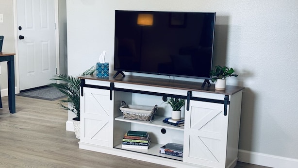 Un meuble de rangement blanc pour appareils multimédias, avec un téléviseur à écran plat, des étagères remplies de livres et d’objets décoratifs, et une plante en pot.