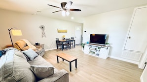 Un salon comprenant un canapé, une table basse, une table à manger avec des chaises, un téléviseur et un ventilateur de plafond.