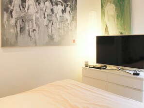 A hotel room with a bed, a flat-screen TV, a white dresser, and a painting on the wall. - studio courtyard in the heart of the 15e (Paris)