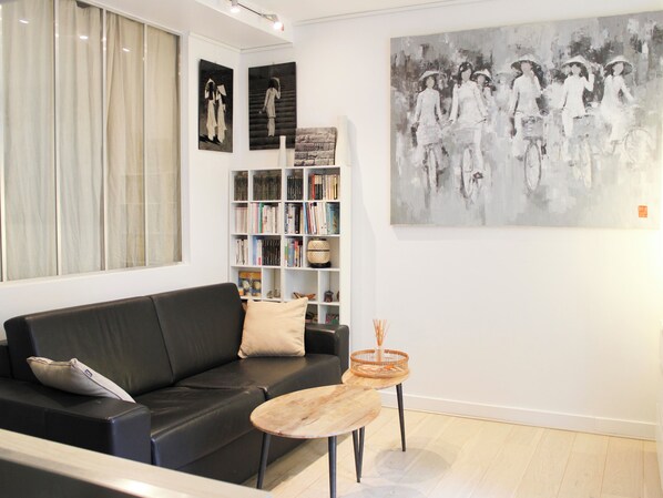 Ein modernes Wohnzimmer mit einem schwarzen Ledersofa, einem kleinen Holztisch, einem Bücherregal und einem großen abstrakten Gemälde an der Wand.