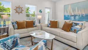 A living room with a sofa, armchairs, a coffee table, and a painting of sailboats.