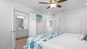 Ein Schlafzimmer mit einem Bett, einem Deckenventilator, einem Gemälde und einem Badezimmer mit Spiegel und Waschbecken.