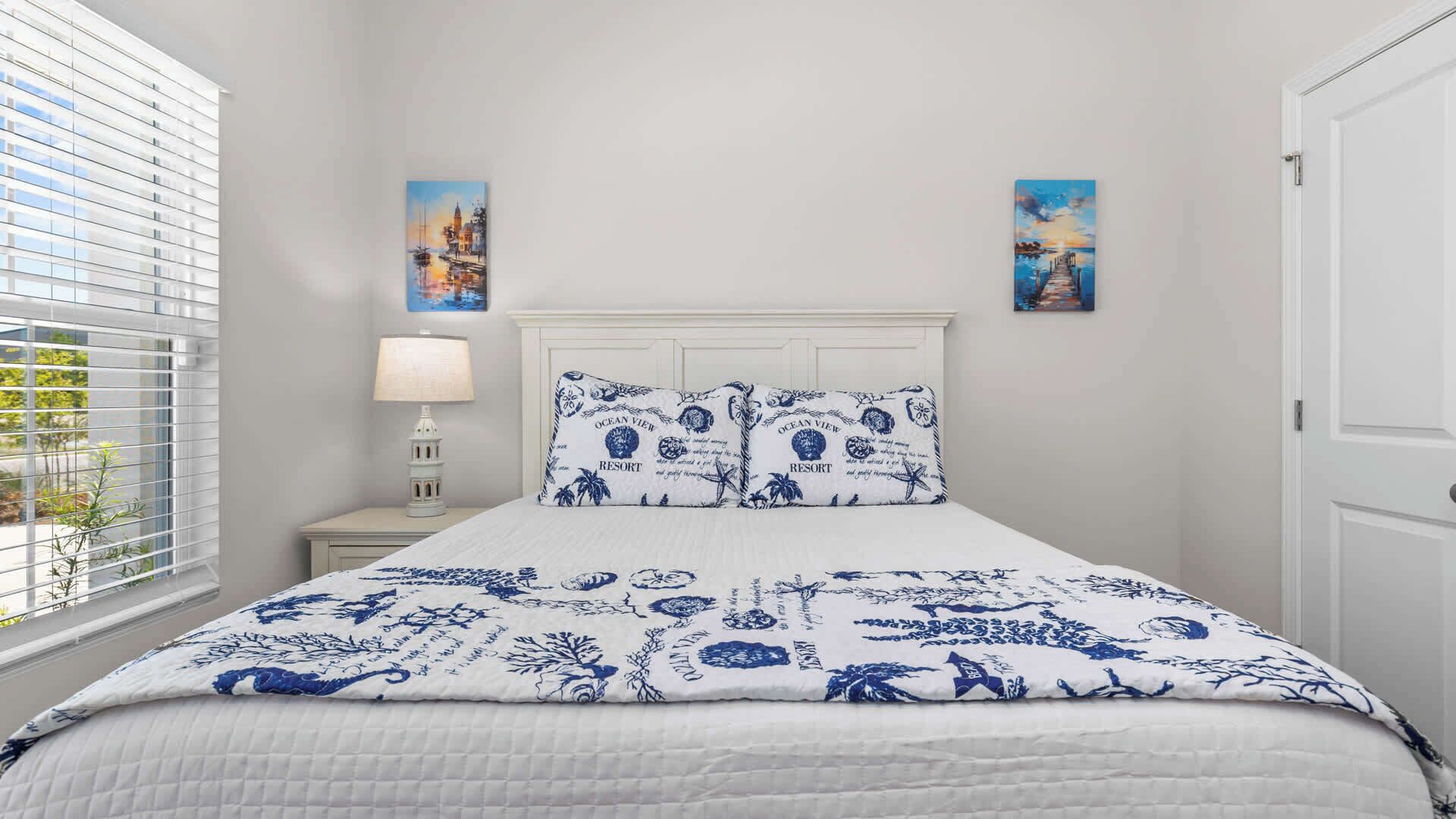 A bedroom with a bed, nightstand, lamp, and two paintings on the wall.