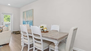Un comedor con mesa de madera, sillas blancas y un cuadro en la pared.