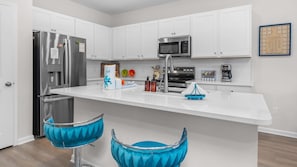 A modern kitchen with white cabinetry, stainless steel appliances, a central island, and blue bar stools.