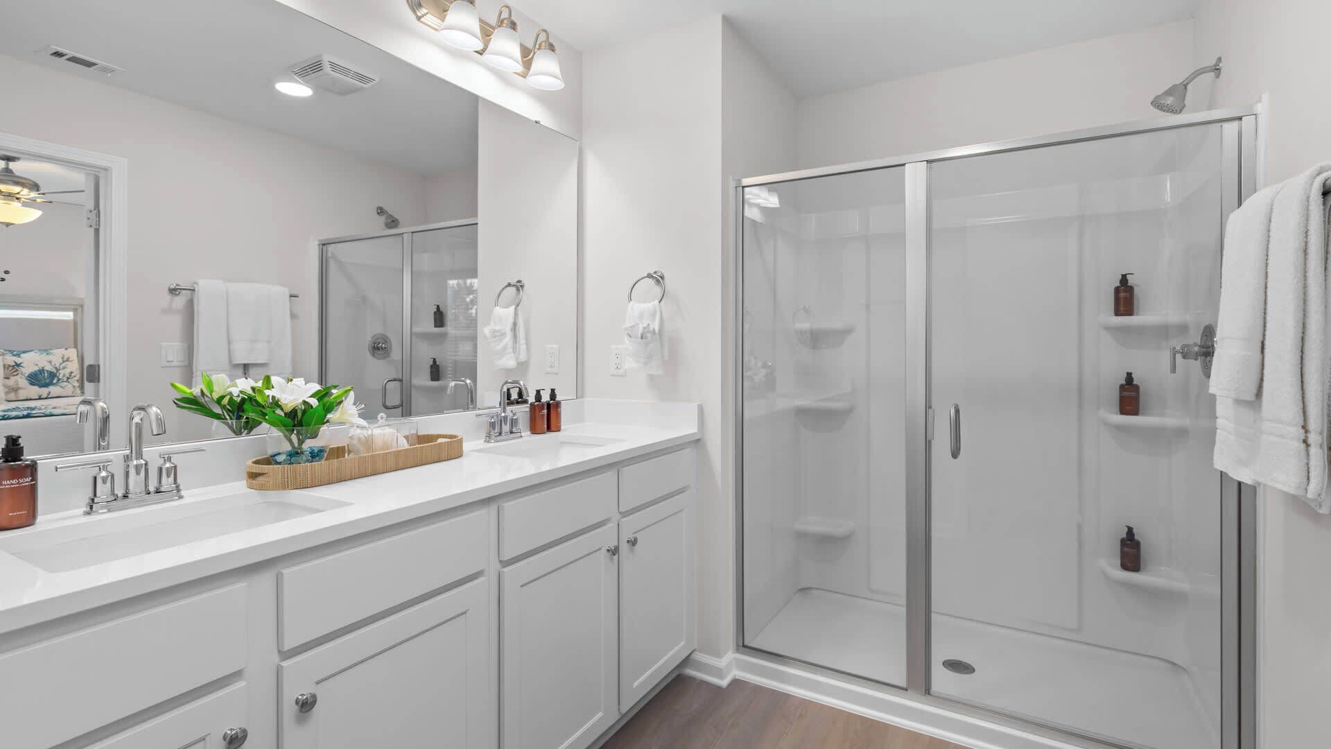 A modern bathroom with a glass shower enclosure, white cabinetry, and a vanity with a mirror.