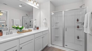 Un baño moderno con cabina de ducha de vidrio, muebles blancos y tocador con espejo.