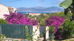 Paesaggio costiero con montagne, mare e un edificio con un cancello e fiori viola.