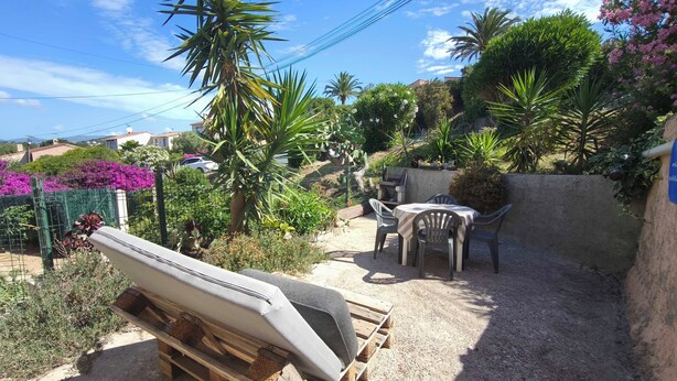 Un'area patio con tavolo e sedie, circondata da diverse piante e una barca su un bancale di legno.