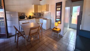 Una cucina compatta con frigorifero, microonde e fornello, un tavolo da pranzo con sedie e un piccolo tavolino con lampada.
