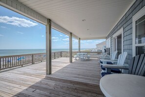 A wooden deck with a railing, white chairs, and a view of the ocean. - Knotty in the Kitchen: Oceanfront Near Park (Oak Island)