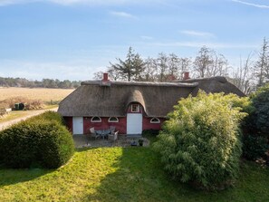 A thatched-roof house with a red door, a small patio with a table and chairs, surrounded by greenery. - 5 Star Holiday Home in Romo (Rømø)