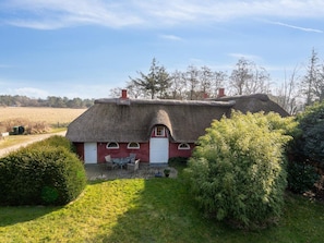Ein Haus mit einem Strohdach, einer roten Tür und einer kleinen Terrasse mit Sitzgelegenheiten.