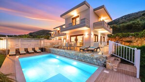 A modern two-story house with a swimming pool, outdoor seating, and a stone wall. - Sunlight Villa Heated Pool (Georgioupoli)