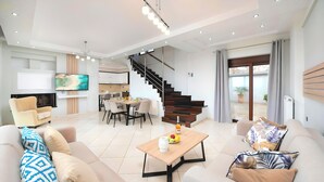 A modern living room with a sofa, coffee table, and a TV. There is a staircase leading to a balcony with a view. - Sunlight Villa Heated Pool (Georgioupoli)