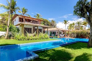 Ein zweistöckiges Haus mit Swimmingpool, umgeben von Palmen und Grünpflanzen.