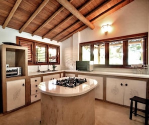 A kitchen with a central island, wooden cabinets, a microwave, and a window with blinds.