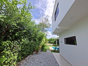 A modern building with a white exterior, a gravel pathway, and a pool in the background.