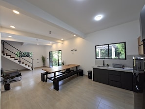 A modern kitchen with a wooden table, a built-in stove, and a window overlooking greenery.