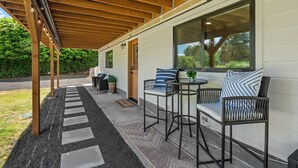 An outdoor covered patio with a seating area, a wooden ceiling, and a large window. - Hidden Harbor Getaway-Sunrise Views-Private Beach Access (Gig Harbor)