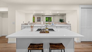 A modern kitchen with a large island, white cabinetry, and a view of greenery outside. - Hidden Harbor Getaway-Sunrise Views-Private Beach Access (Gig Harbor)