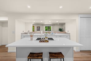 Una cocina moderna con una isla grande, armarios blancos y vistas a zonas verdes.
