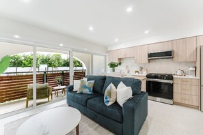 A modern kitchen with a built-in oven and microwave, a dining area with a table and chairs, and a large sliding glass door leading to an outdoor patio with a view of greenery. - Villa Solana: Boca Pool Hideaway (Boca Raton)