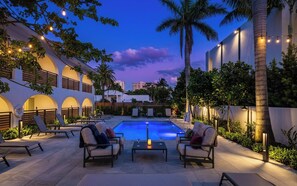 A poolside area with lounge chairs, a table, and string lights. - Villa Solana: Boca Pool Hideaway (Boca Raton)