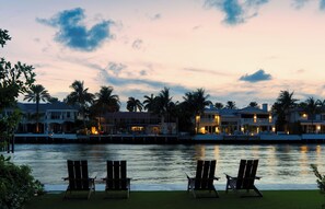 A waterfront property with multiple buildings, a calm body of water, and three lounge chairs. - Villa Solana: Boca Pool Hideaway (Boca Raton)