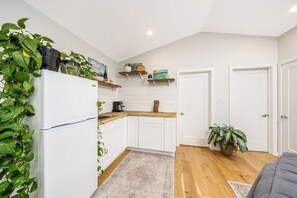 A kitchen with white cabinets, wooden countertops, and a refrigerator. There are plants on the countertops and shelves, and a door to the right.