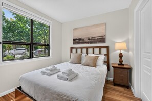 Ein ordentlich bezogenes Bett mit weißen Leinen und gefalteten Handtüchern, ein Holz-Kopfteil, ein Nachttisch mit Lampe und ein Gemälde über dem Bett.