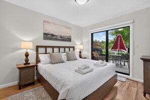 Ein Schlafzimmer mit Bett, Nachttischen, einem Gemälde und Blick durch eine Schiebetür auf einen Außenbereich.