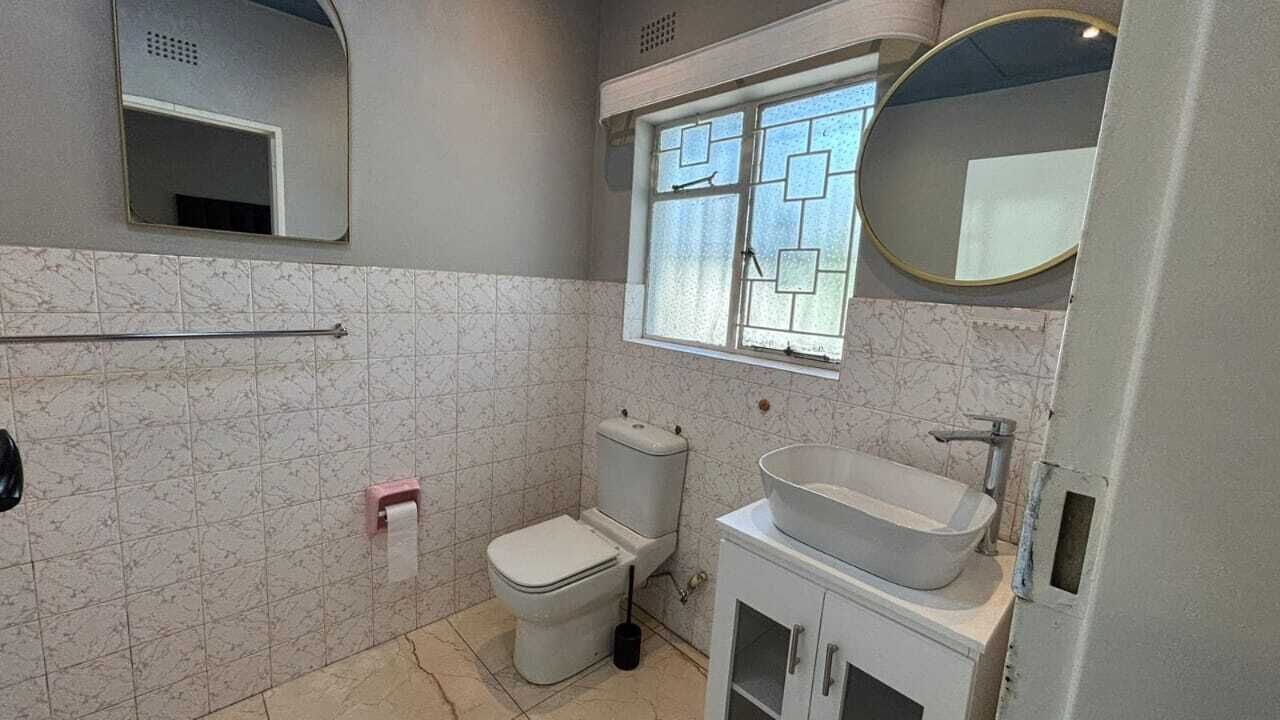 A bathroom with a toilet, a sink, a mirror, and a window with a geometric pattern.