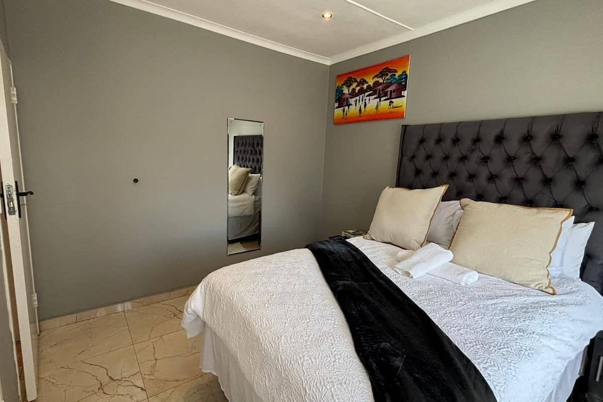 Ein Schlafzimmer mit Bett, Kopfstütze, Spiegel und einem Gemälde an der Wand.