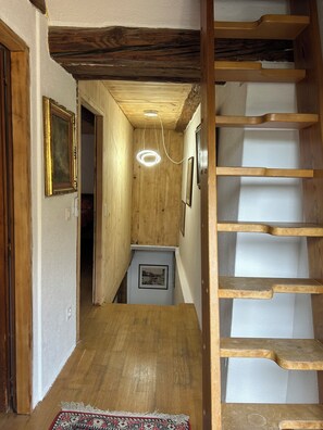 A wooden staircase leading to a second floor, a hallway with wooden walls, a framed picture on the wall, and a small table with a picture on it.