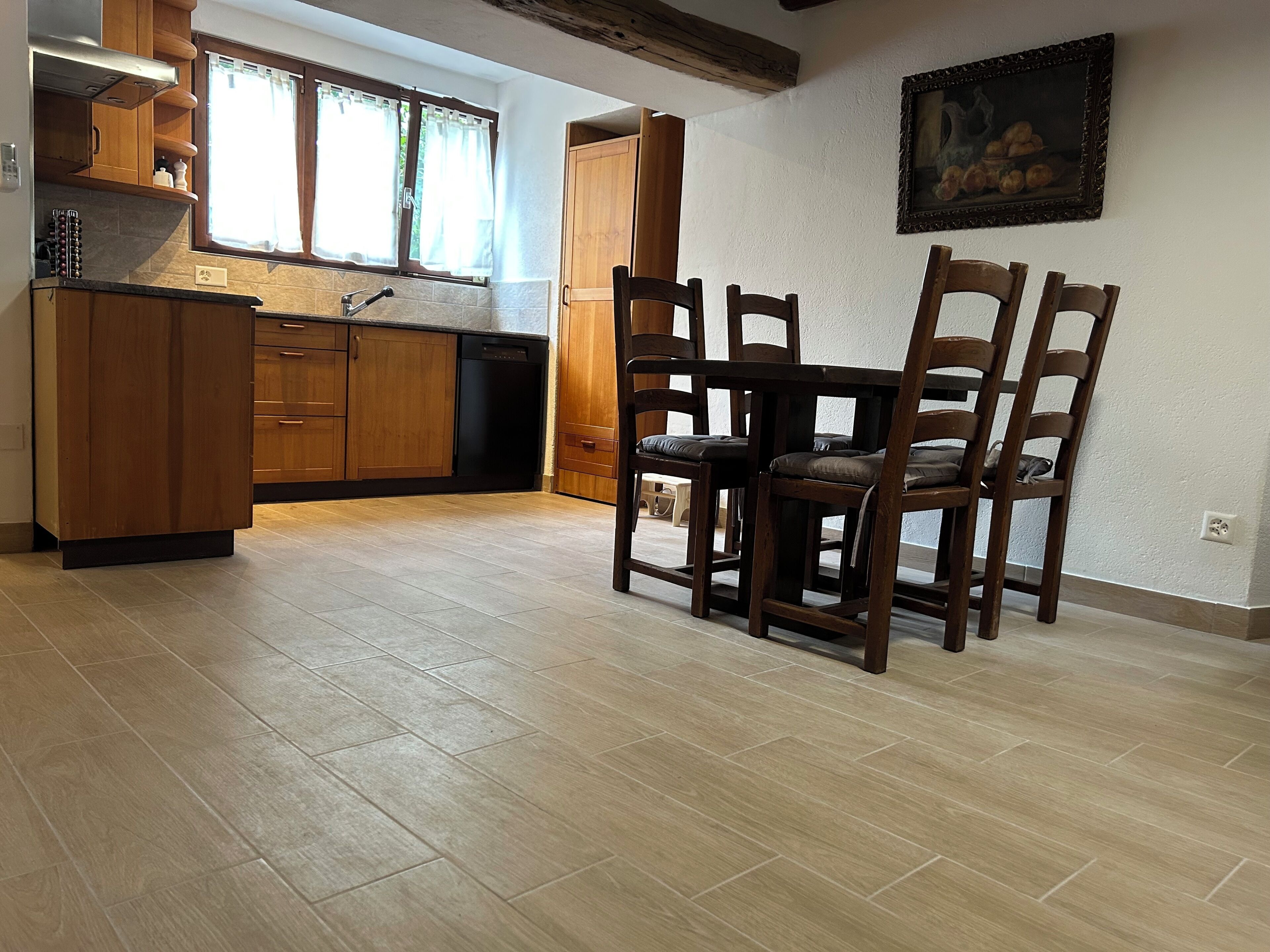 Una cocina con armarios de madera, un lavavajillas negro y una zona de comedor con mesa y sillas de madera.