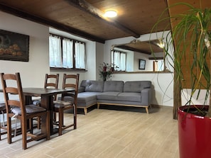 Une pièce comprenant une table à manger en bois, quatre chaises, un canapé gris, une plante en pot rouge et un plafond en bois.