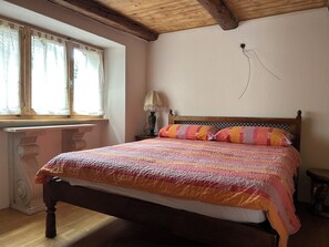 Un lit avec une couverture colorée, une tête de lit en bois, une lampe de chevet et une fenêtre avec des rideaux.