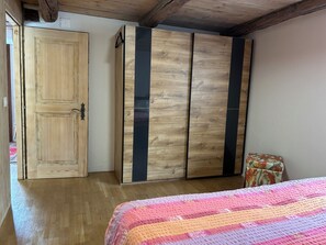 A bedroom with a wooden door, a wardrobe with vertical black stripes, a floral-patterned chair, and a bed with a striped blanket.