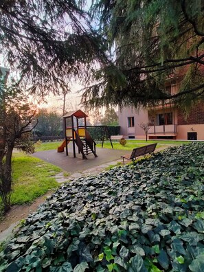 Ein Spielplatz mit Rutsche und Klettergerüst, umgeben von viel Grün und einer Bank.
