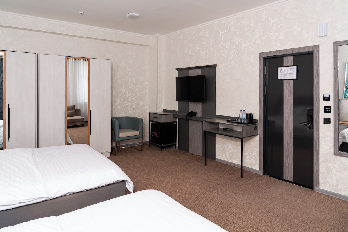 A hotel room with a bed, a desk, a chair, a television, and a wardrobe.