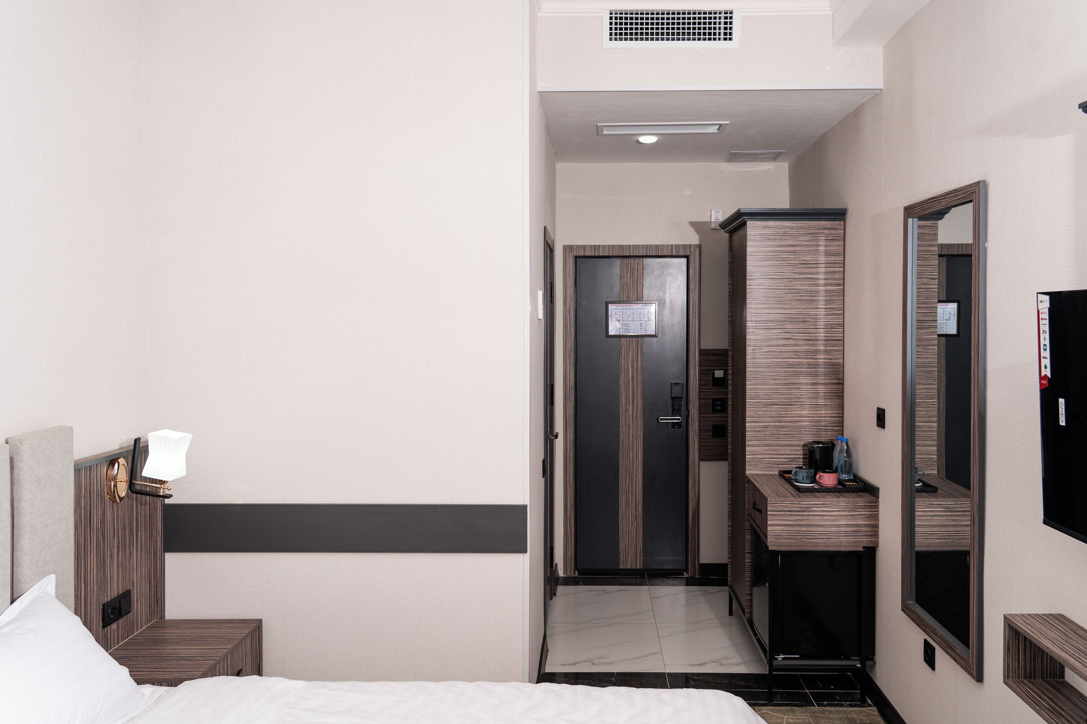 A hotel room with a bed, a bedside table, a mirror, a wardrobe, and a small desk with a chair.