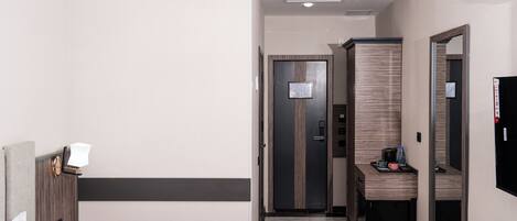 A hotel room with a bed, a bedside table, a mirror, a wardrobe, and a small desk with a chair.