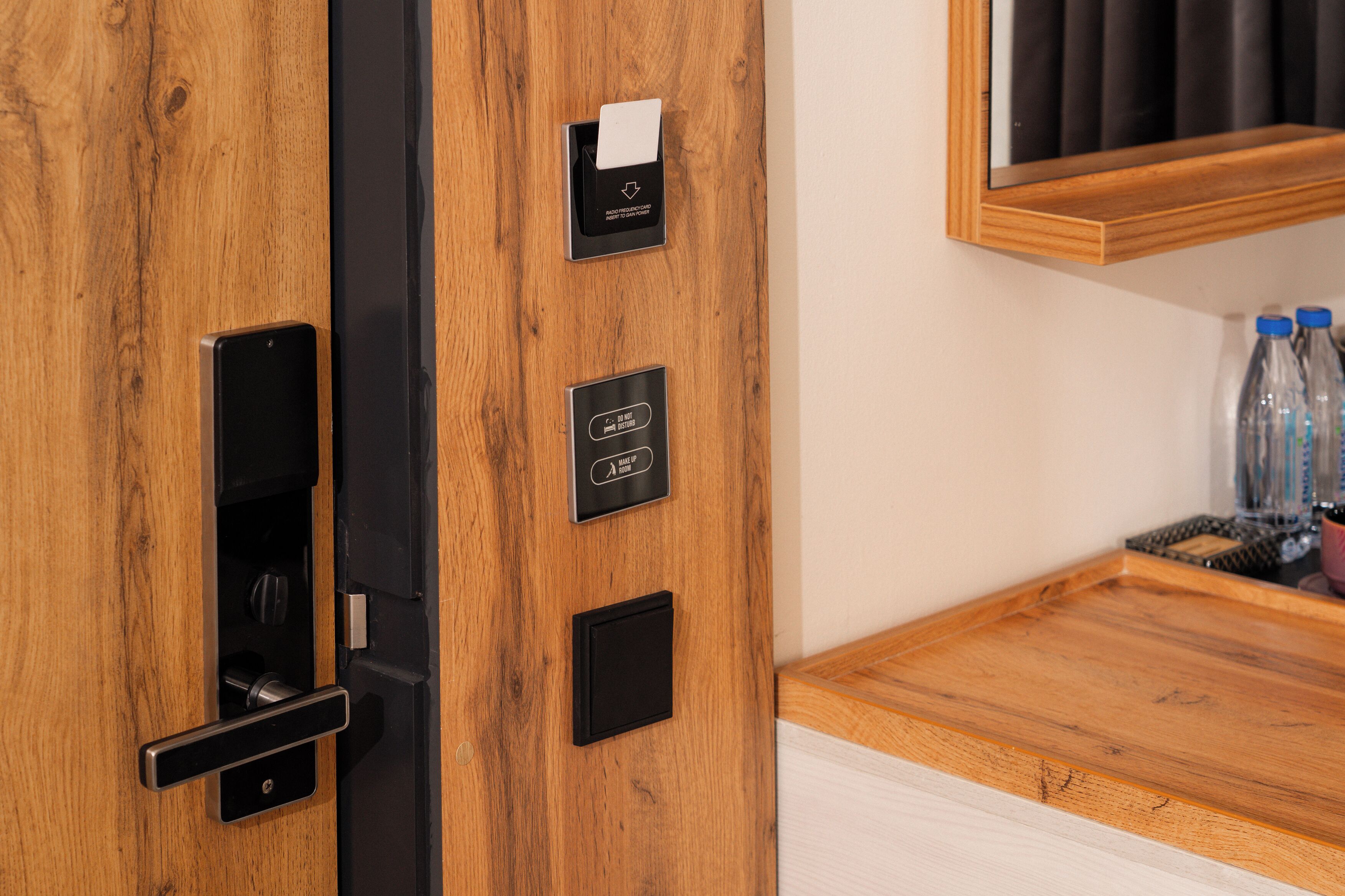 A wooden door with a keycard reader, a room number plaque, and a small black panel.