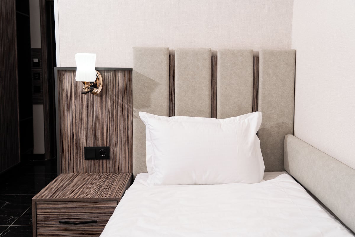 A neatly made bed with a white pillow and a headboard with vertical slats.