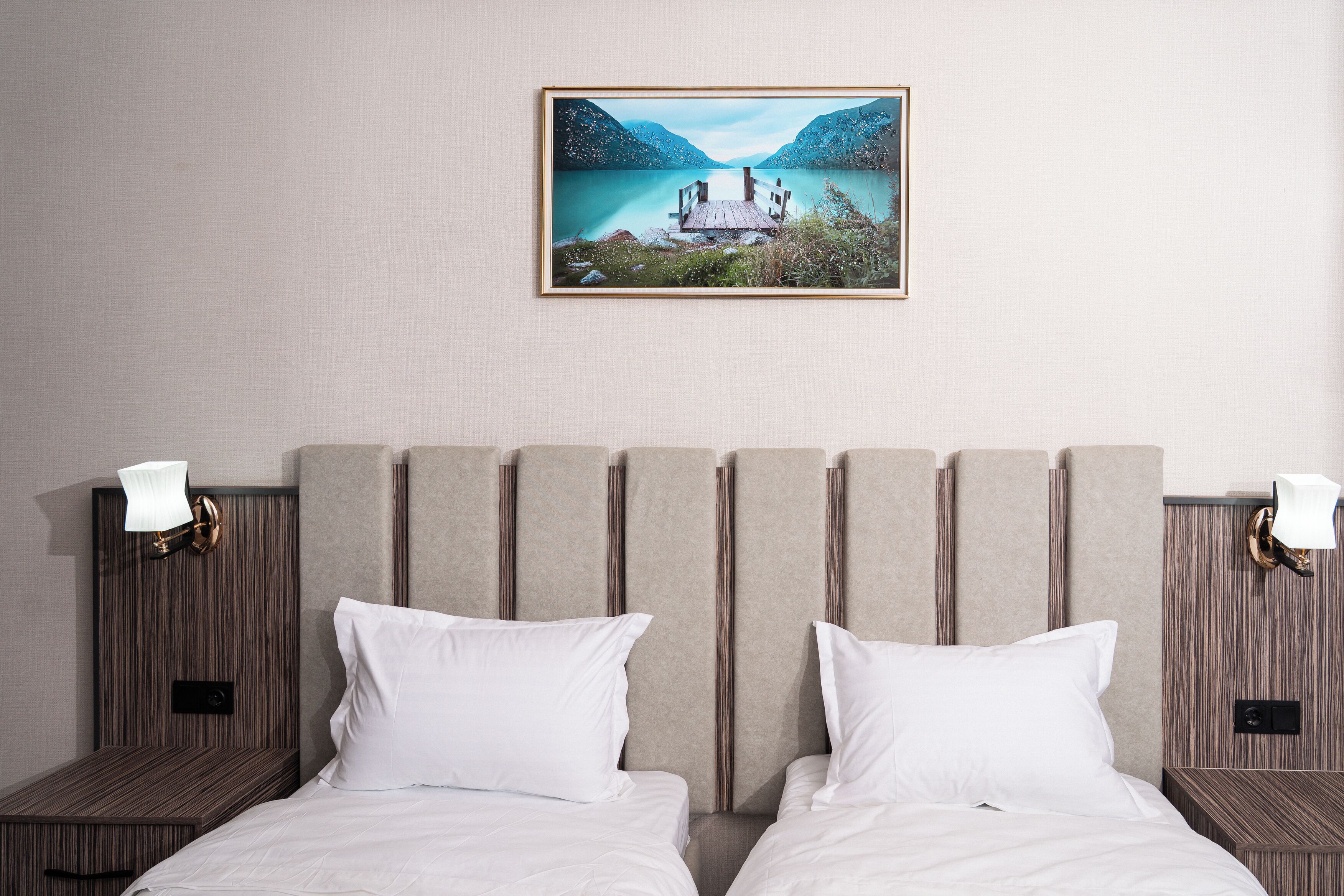 A double bed with a wooden headboard, two bedside tables with lamps, and a framed landscape painting above.