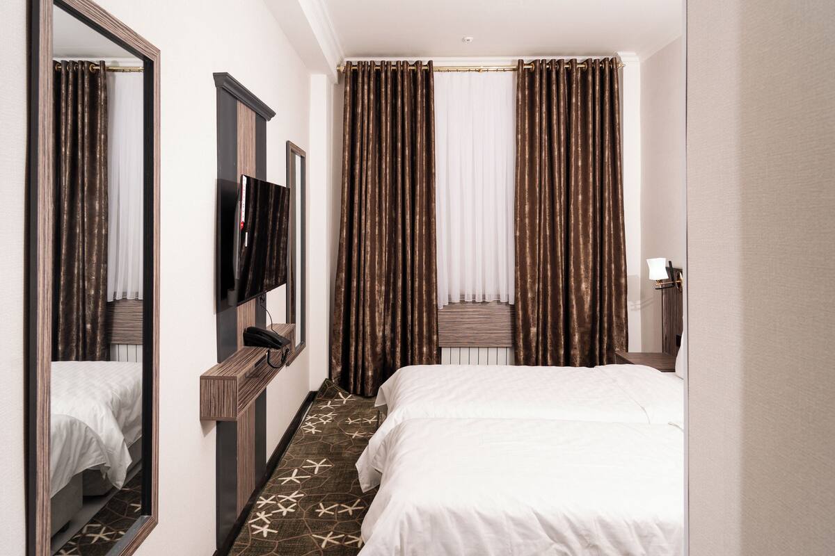 A hotel room with a bed, a TV, a mirror, a desk, and a window with curtains.