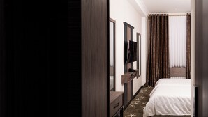 A hotel room with a bed, a TV, a mirror, a wardrobe, and a patterned carpet. - Gulshan Hotel (Urgench)